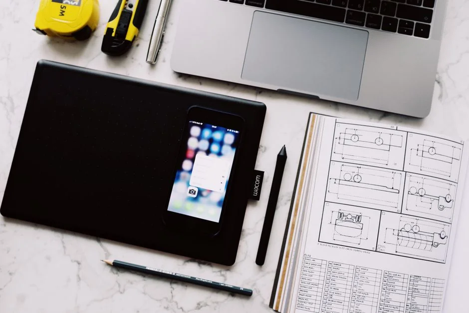 A top-down view of a minimalist workspace featuring a laptop and blank paper on a wooden table.